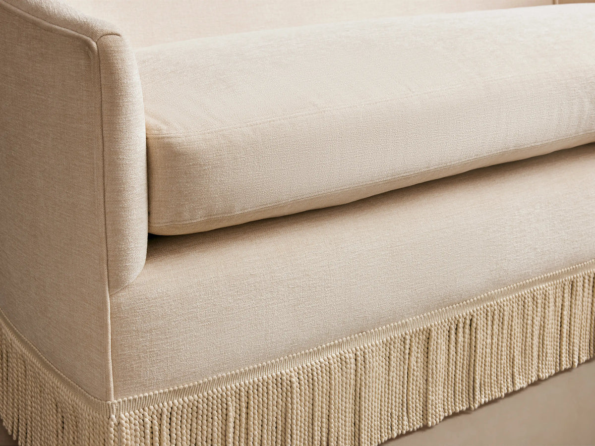 Off-white Giles Settee with Fringe, a curved two-seater sofa with a long, light-colored fringe along its base.
