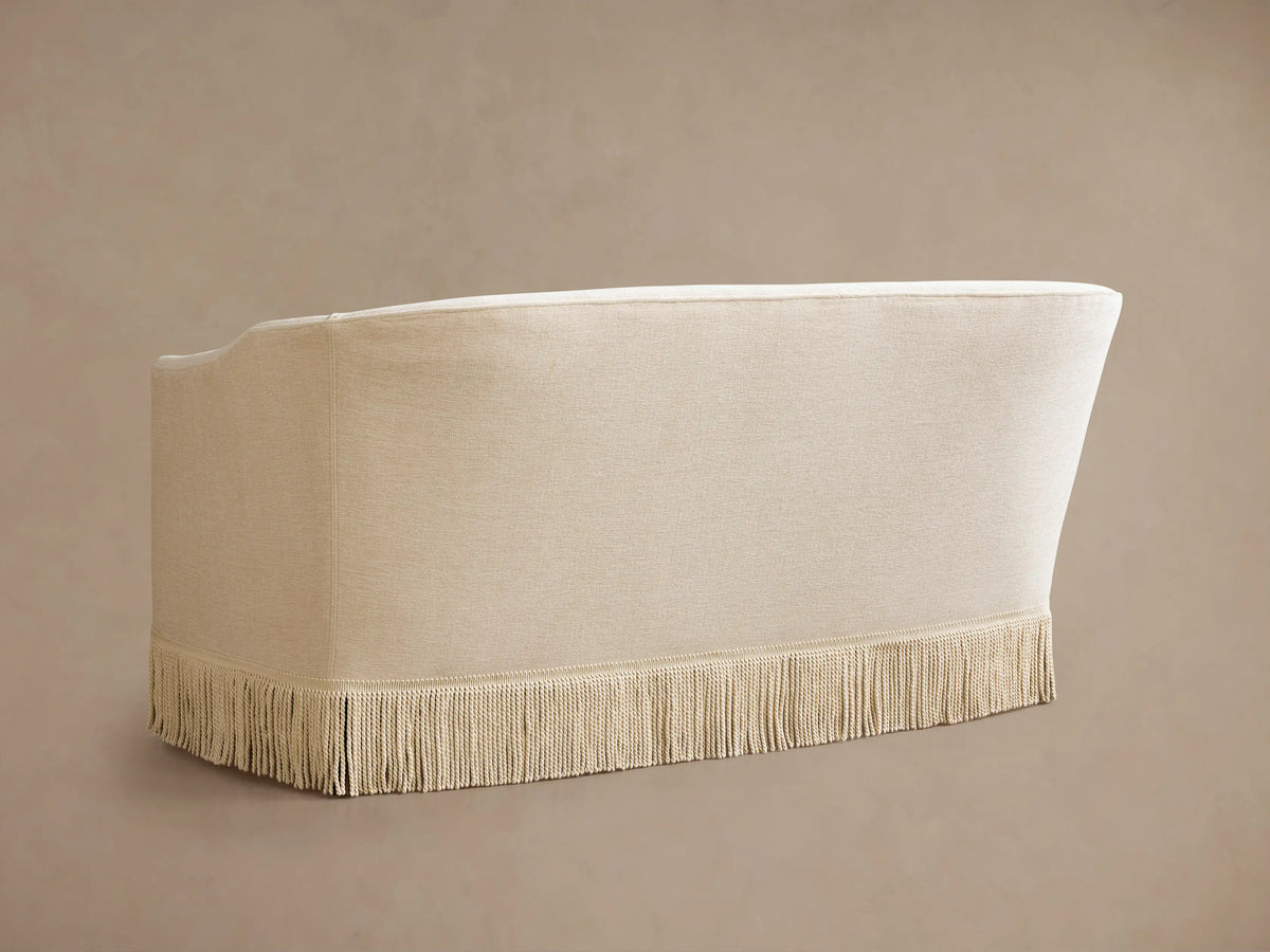 Close-up of Giles Settee with Fringe. Cream-colored fabric, soft cushions, and elegant beaded fringe along the bottom edge.