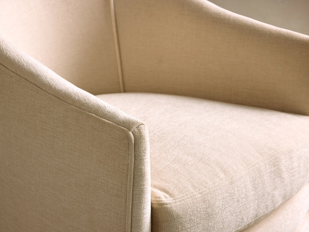 Cream upholstered Giles Swivel Chair with a curved back, thick seat cushion, and a full fringed skirt, seen from the front.