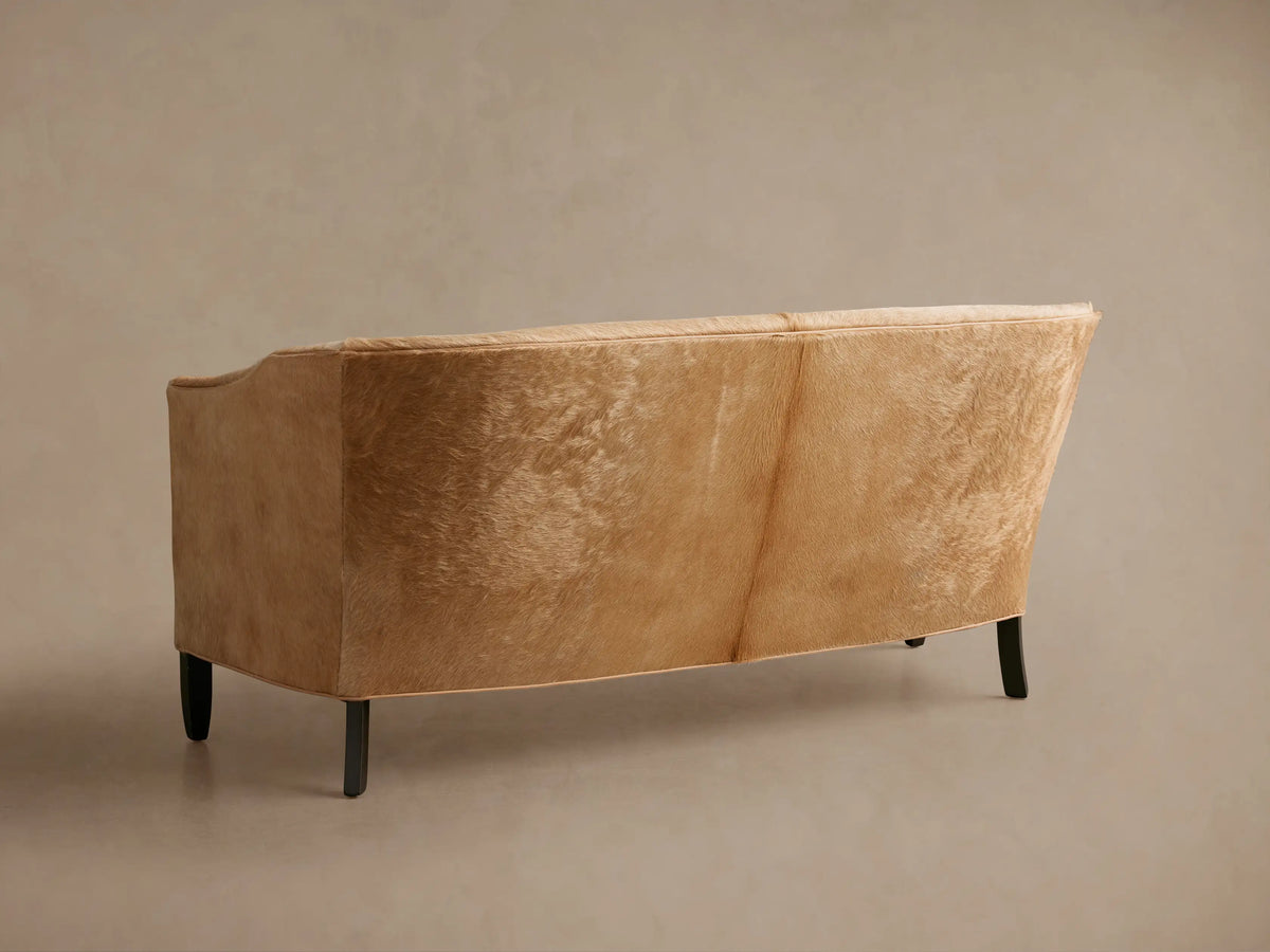 Angled front view of the Tan Giles Hair on Hide Settee, highlighting its curved arm, back, and soft, short-haired upholstery.