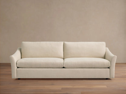Helena Sofa: Front view of a light cream fabric sofa with two plump seat cushions, gently curved arms, on a wooden floor.