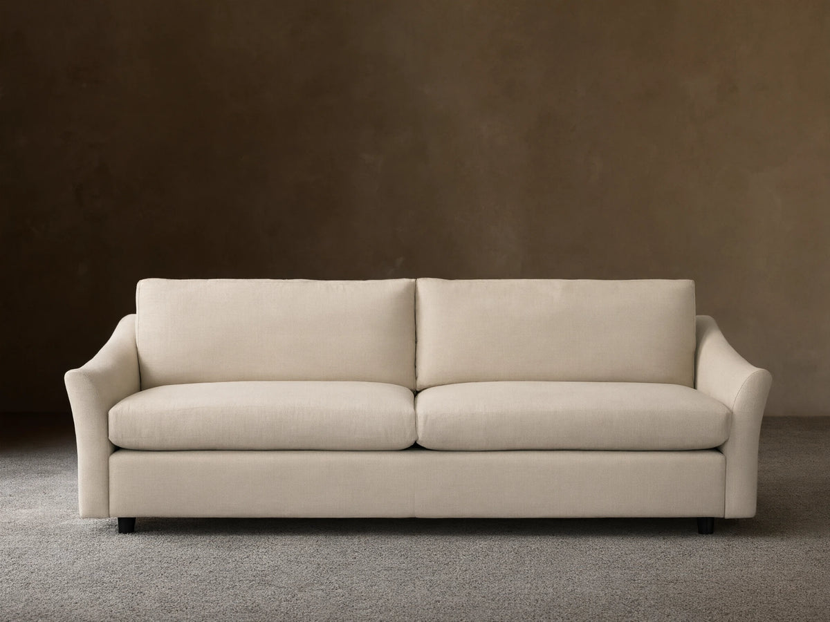 Helena Sofa: Front view of a light cream fabric sofa with two plump seat cushions, gently curved arms, on a wooden floor.