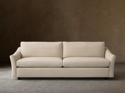 Helena Sofa: Front view of a light cream fabric sofa with two plump seat cushions, gently curved arms, on a wooden floor.