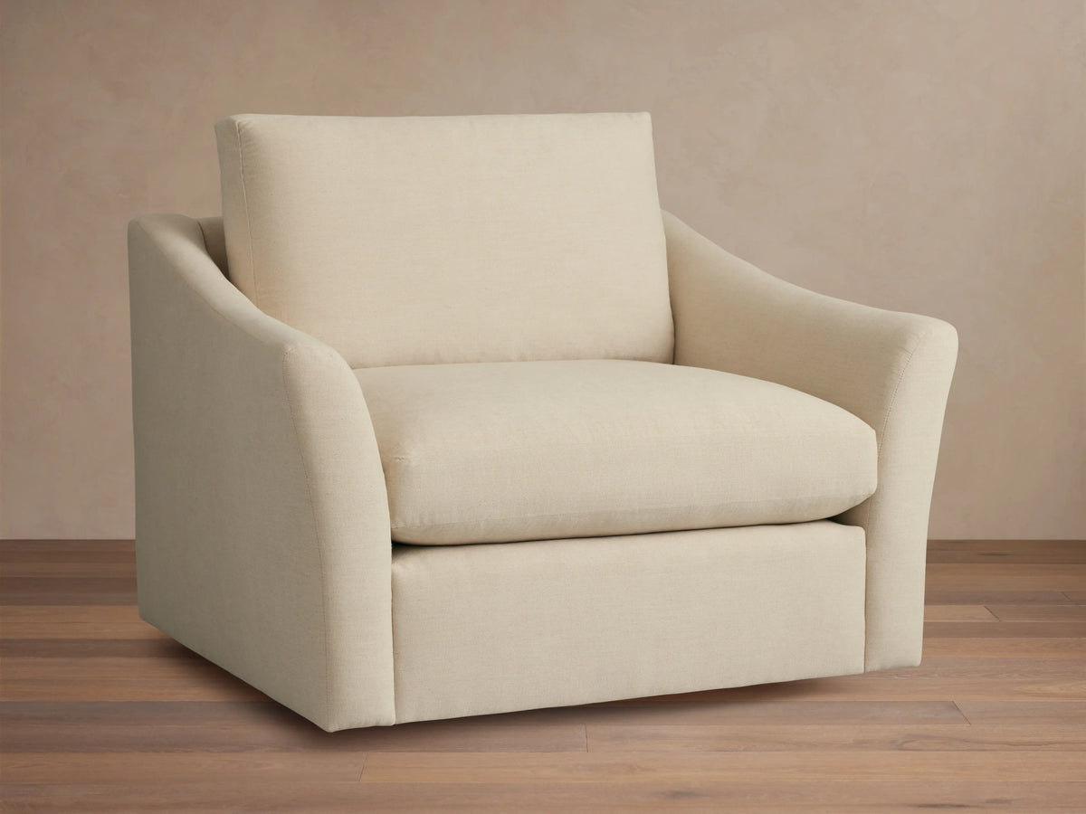 Helena Swivel Chair in beige fabric, features gently curved armrests and a cushioned seat and backrest on a wooden floor background.