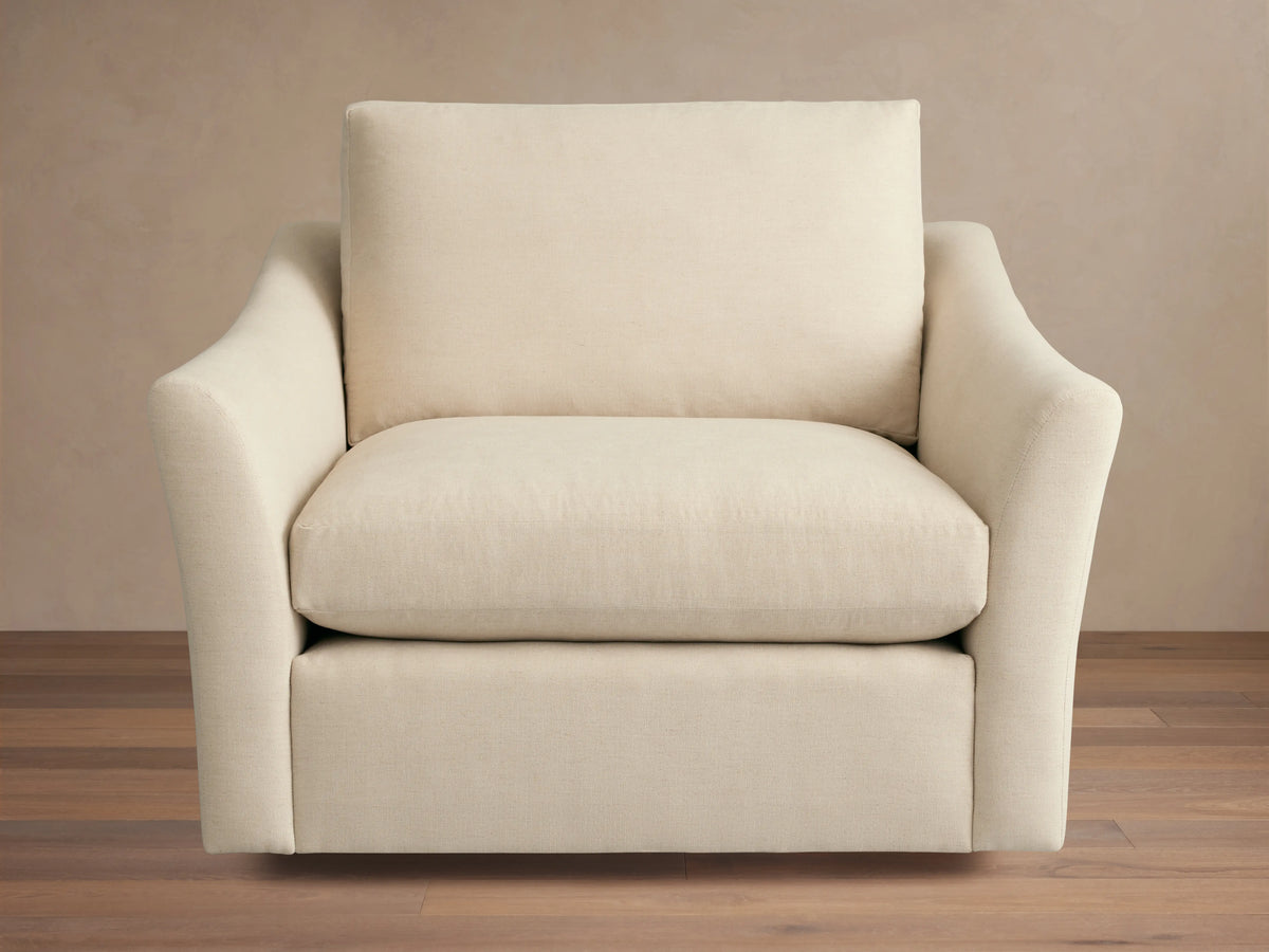 Helena Swivel Chair in beige fabric, features gently curved armrests and a cushioned seat and backrest on a wooden floor background.