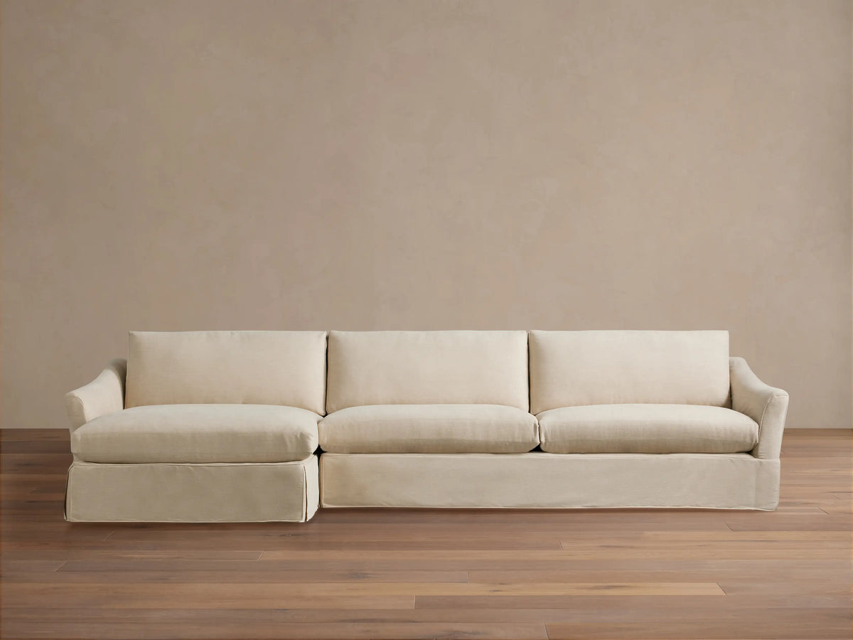 Helena Slipcovered Two Piece Chaise Sectional in light cream fabric, left-facing chaise, skirted base, on wood floor.