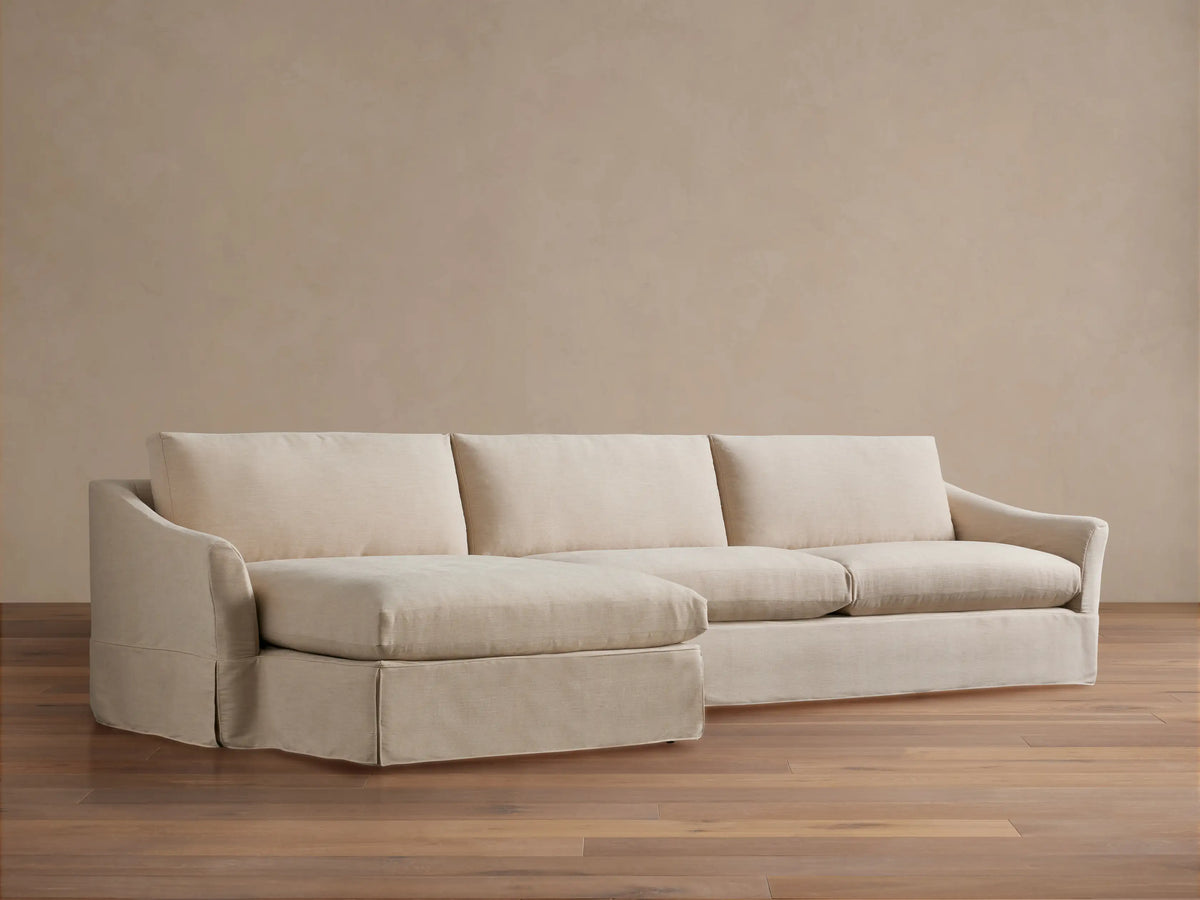 Helena Slipcovered Two Piece Chaise Sectional in light cream fabric, left-facing chaise, skirted base, on wood floor.