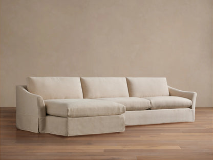 Helena Slipcovered Two Piece Chaise Sectional in light cream fabric, left-facing chaise, skirted base, on wood floor.