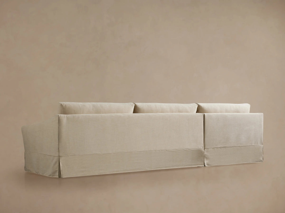 Helena Slipcovered Two Piece Chaise Sectional. Close-up of the light beige chaise cushion, curved armrest, and slipcover base.