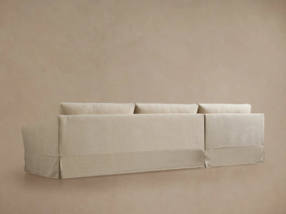 Helena Slipcovered Two Piece Chaise Sectional. Close-up of the light beige chaise cushion, curved armrest, and slipcover base.
