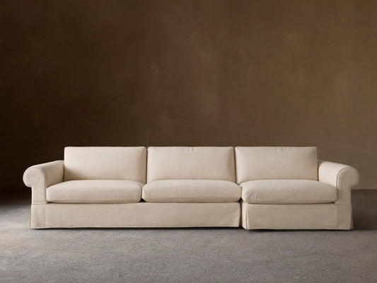 Helena Slipcovered Two Piece Chaise Sectional in light cream fabric, left-facing chaise, skirted base, on wood floor.