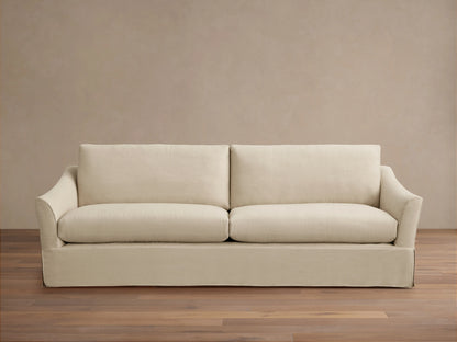 Helena Slipcovered Sofa in a beige fabric, featuring a clean silhouette, low arms, and plush cushions on a wooden floor.