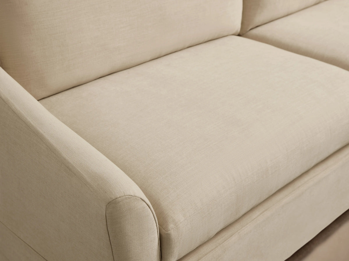 Helena Slipcovered Sofa in a beige fabric, featuring a clean silhouette, low arms, and plush cushions on a wooden floor.