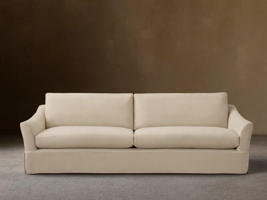 Helena Slipcovered Sofa in a beige fabric, featuring a clean silhouette, low arms, and plush cushions on a wooden floor.