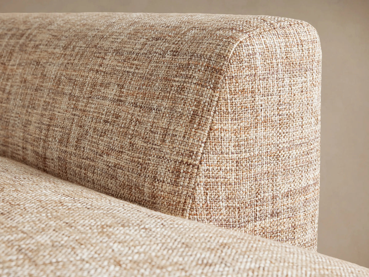Hamlin Daybed, back and side view, upholstered in light brown textured fabric, with rounded modern design against a plain wall.