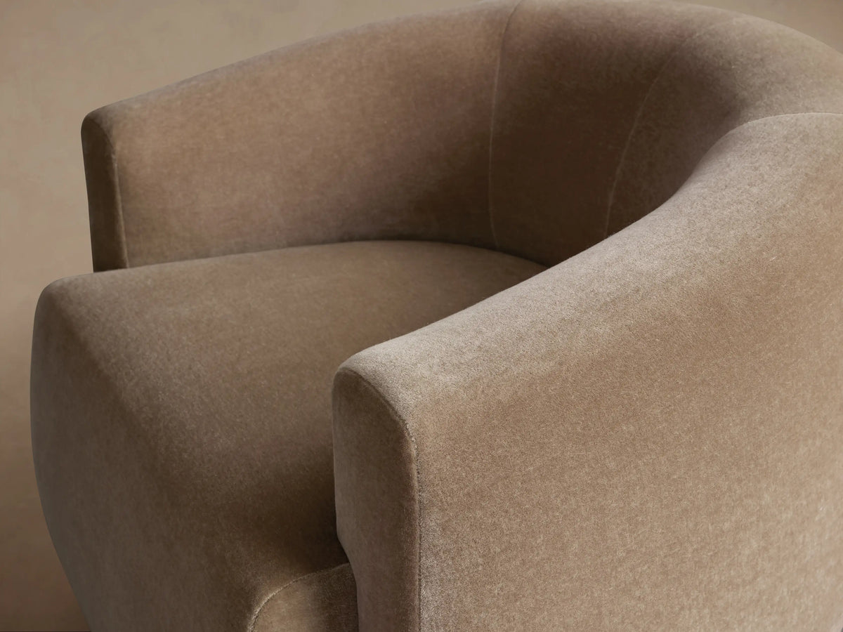Front view of a round, taupe Hamlin Swivel Chair with curved back and arms, upholstered in soft fabric, sitting on a wooden floor.