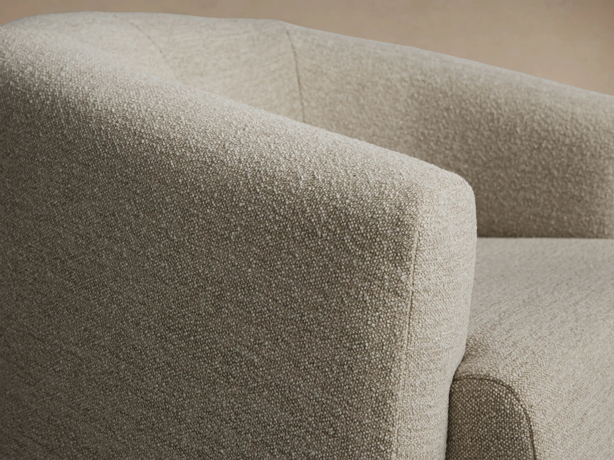 Hamlin Swivel Chair, upholstered in textured light beige fabric, with a rounded back and arms, on a wooden floor.