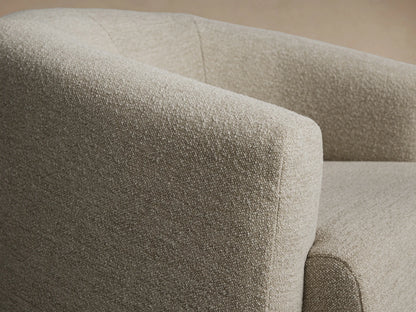 Hamlin Swivel Chair, upholstered in textured light beige fabric, with a rounded back and arms, on a wooden floor.