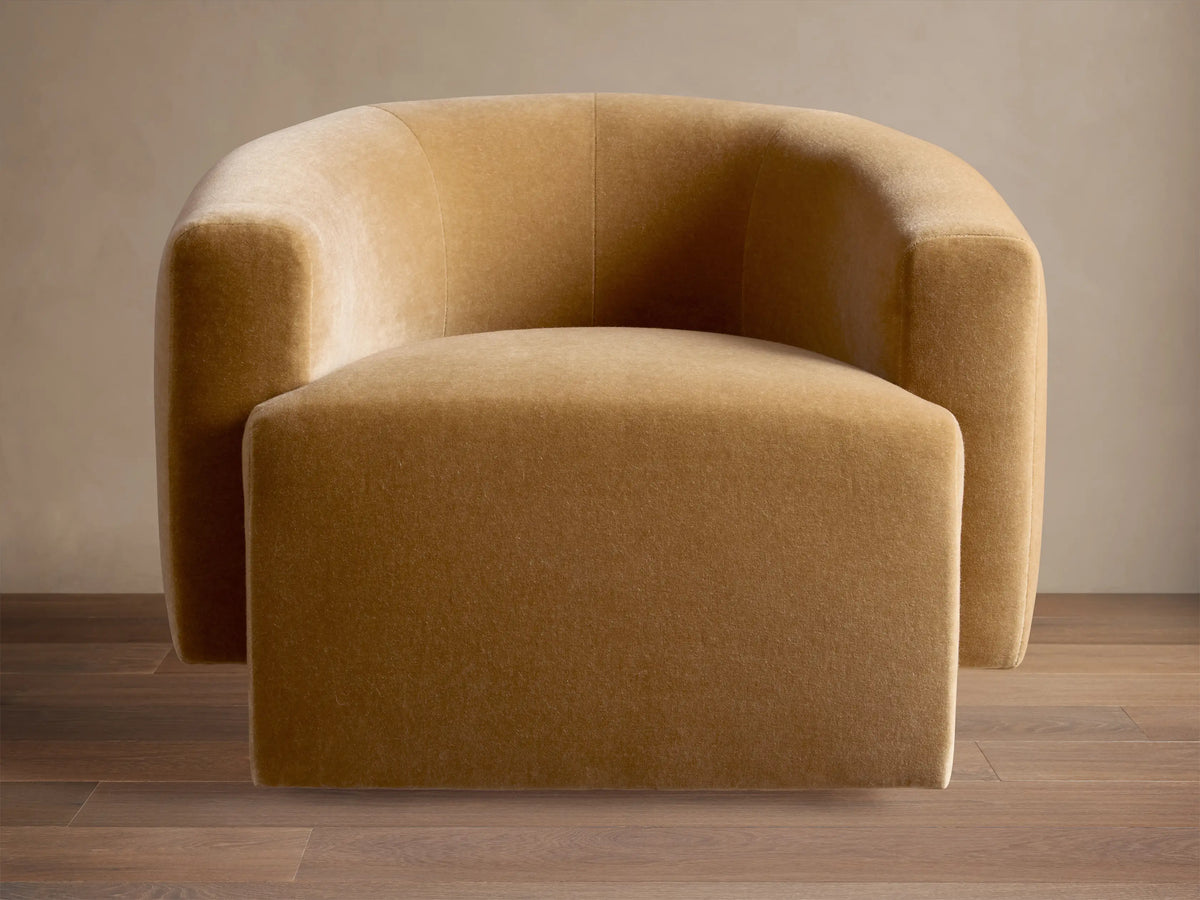 Two caramel Hamlin Swivel Chairs™ with curved backs, in a sunlit living room with a blue floral sectional.