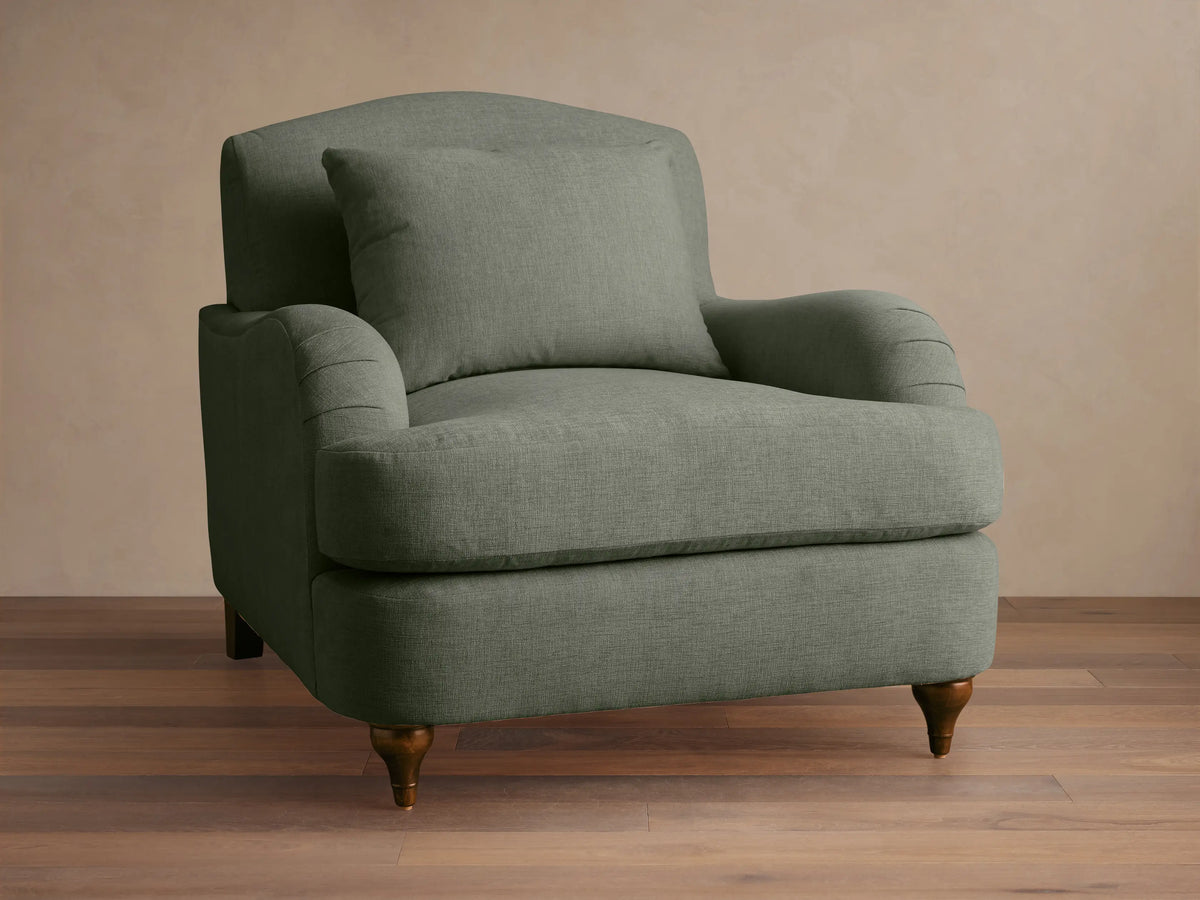 Sage green Hanover Chair with curved back, plush seat, pleated rolled arms, and dark turned wood legs on a wood floor.