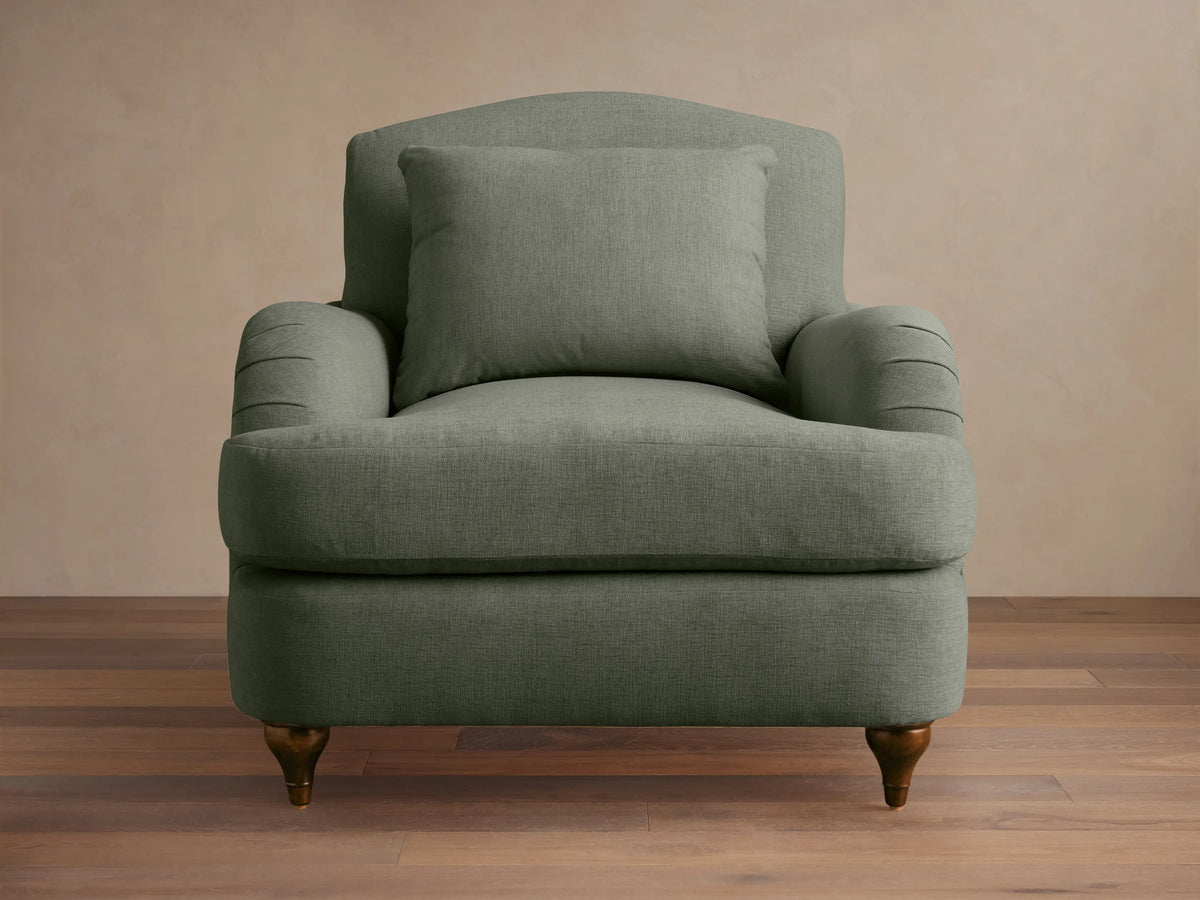 Sage green Hanover Chair with curved back, plush seat, pleated rolled arms, and dark turned wood legs on a wood floor.