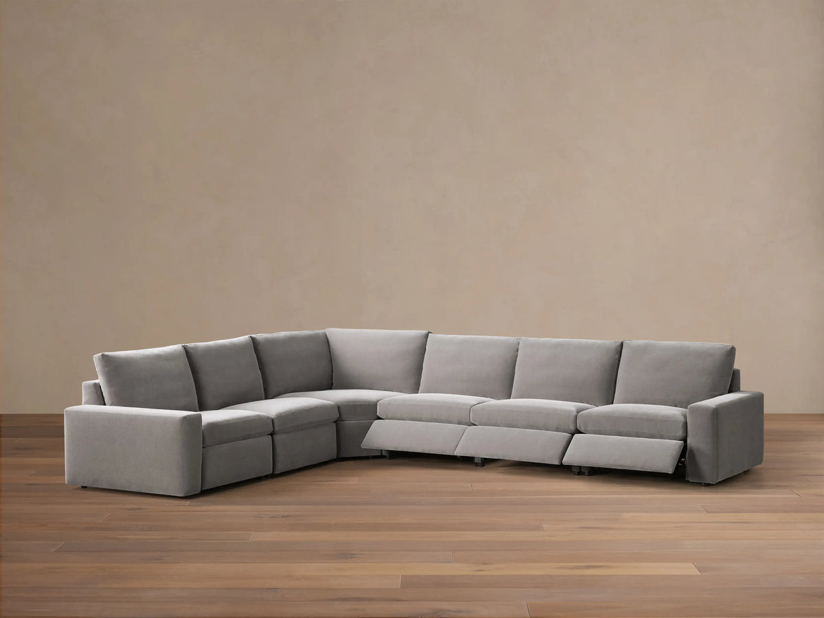 Front view of a grey Kipton Wide Arm Six Piece Motion Sectional, featuring wide arms and one seat reclined with footrest extended.