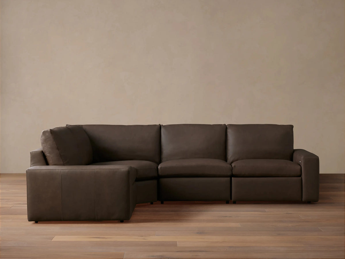 Dark brown leather Kipton Wide Arm Four-Piece Motion Sectional, L-shaped, on wood floor against light wall.