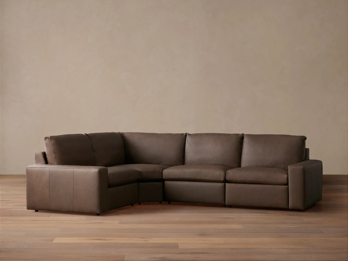 Dark brown leather Kipton Wide Arm Four-Piece Motion Sectional, L-shaped, on wood floor against light wall.