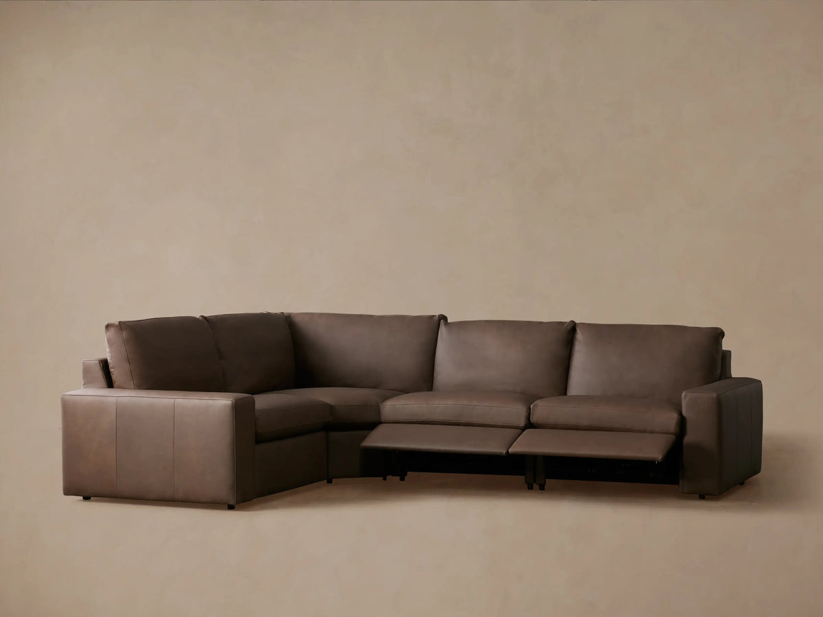 Rear-right view of Kipton Wide Arm Leather Four-Piece Motion Sectional. L-shaped, four-piece taupe leather sofa with raised back cushions.