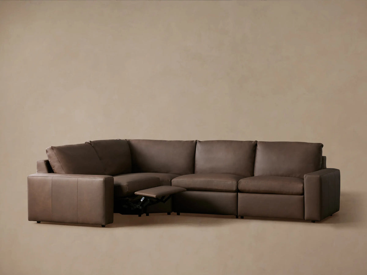 Kipton Wide Arm L-shaped four-piece motion sectional in brown leather, two footrests extended, against a neutral wall.