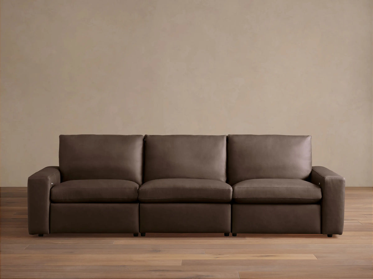 Kipton Wide-Arm Leather Three-Piece Motion Modular Sofa in rich dark brown, with plump cushions, on a wood floor.