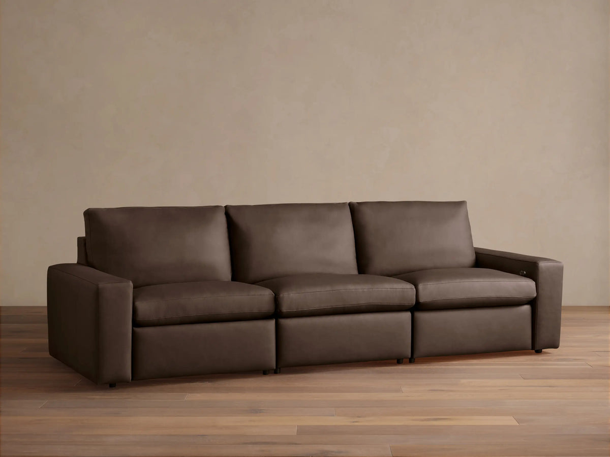 Kipton Wide-Arm Leather Three-Piece Motion Modular Sofa in rich dark brown, with plump cushions, on a wood floor.