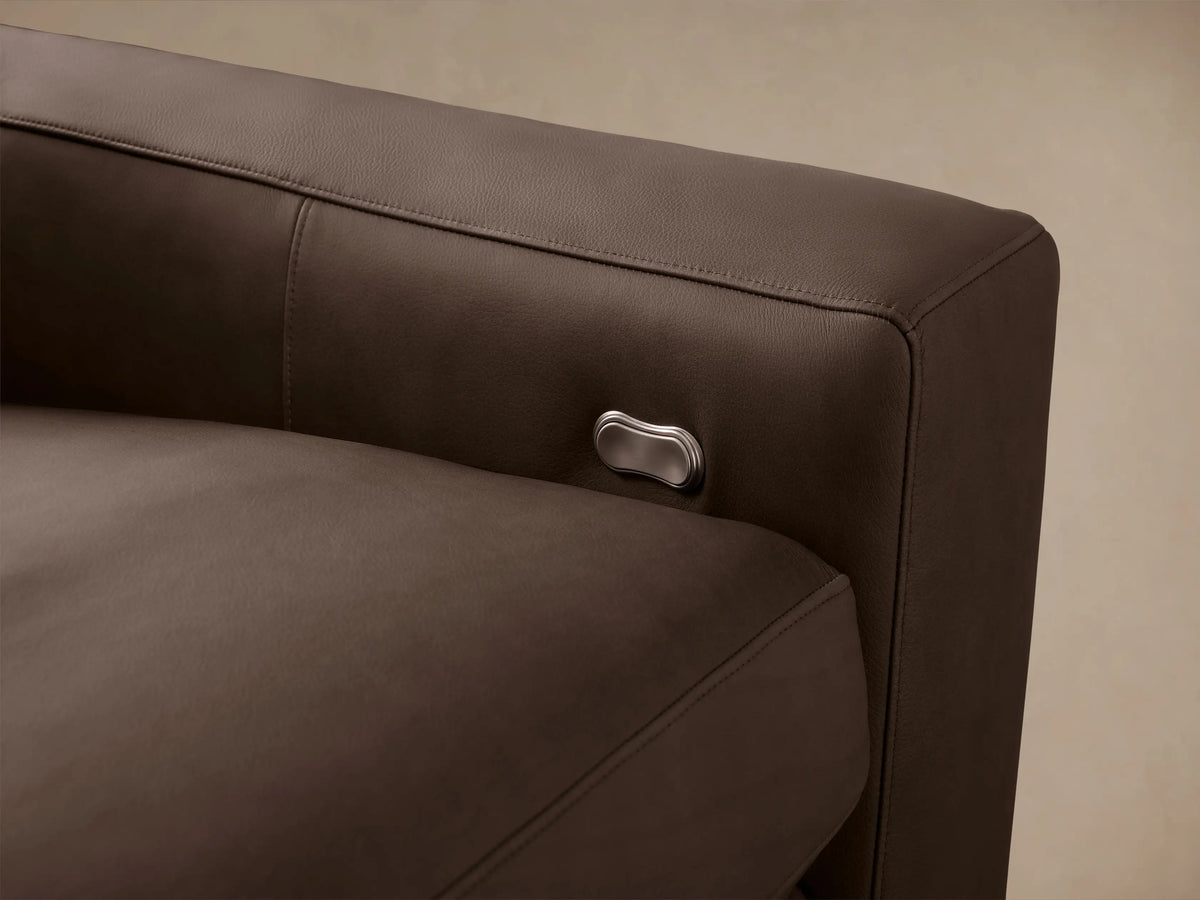 Kipton 3-piece modular motion sofa in rich taupe leather, wide arms, against a beige wall & wood floor.