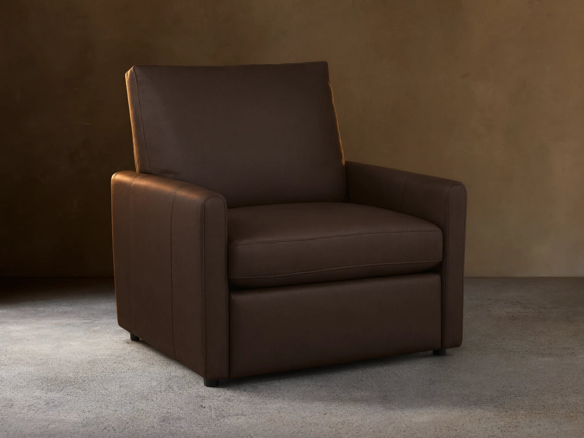 A dark brown Kipton Leather Motion Recliner with a sleek design. Features smooth leather, slim arms, and cushioned backrest on a wooden floor.