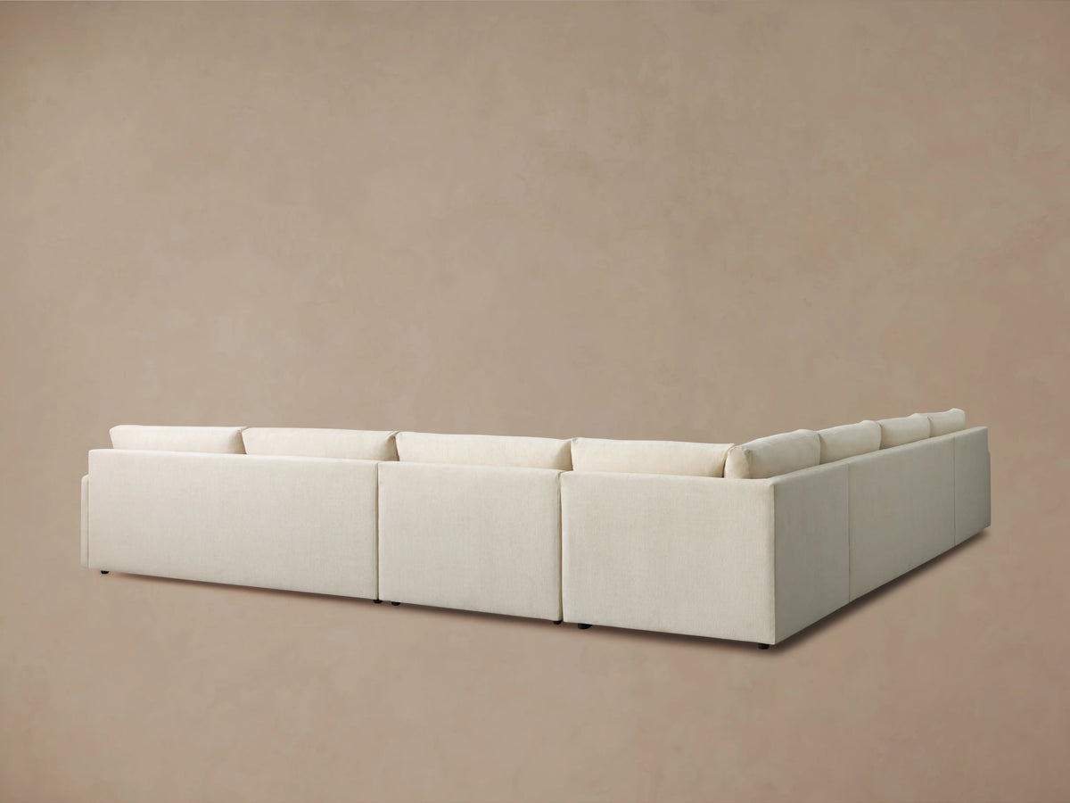 Kipton Slim Arm Five-Piece Chaise Sectional in light cream fabric, viewed from the back-right against a beige wall.
