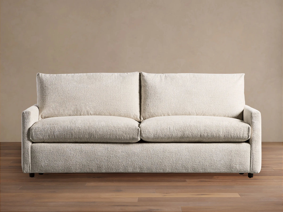 Off-white Kipton Slim Arm Sleeper Sofa with textured fabric, two seat cushions, two back cushions, on a wood floor.