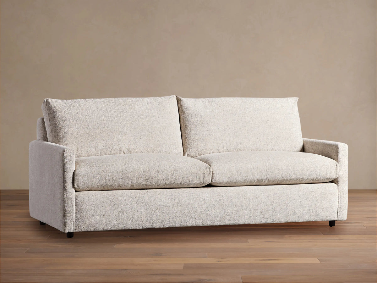 Off-white Kipton Slim Arm Sleeper Sofa with textured fabric, two seat cushions, two back cushions, on a wood floor.