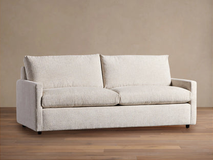 Off-white Kipton Slim Arm Sleeper Sofa with textured fabric, two seat cushions, two back cushions, on a wood floor.