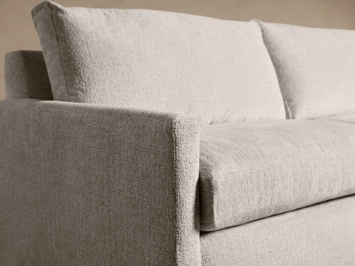 Kipton Slim Arm Sleeper Sofa, light cream textured fabric. Front view on a wooden floor.
