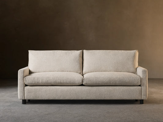 Off-white Kipton Slim Arm Sleeper Sofa with textured fabric, two seat cushions, two back cushions, on a wood floor.