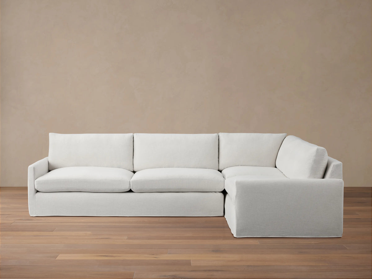 A light grey Kipton Slipcovered Two-Piece Sectional with a right-facing chaise. It has a soft, tailored appearance on a wooden floor.