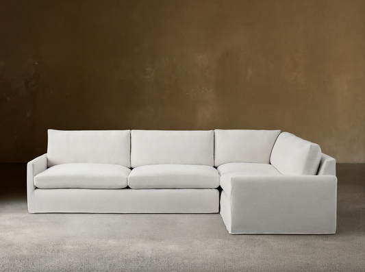 A light grey Kipton Slipcovered Two-Piece Sectional with a right-facing chaise. It has a soft, tailored appearance on a wooden floor.