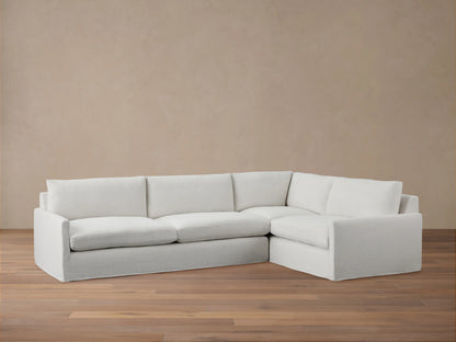 A light grey Kipton Slipcovered Two-Piece Sectional with a right-facing chaise. It has a soft, tailored appearance on a wooden floor.