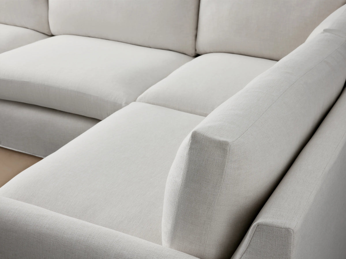 Kipton Slipcovered Two-Piece Sectional in a light beige fabric, featuring a left-arm sofa and right-arm corner piece on a wooden floor.