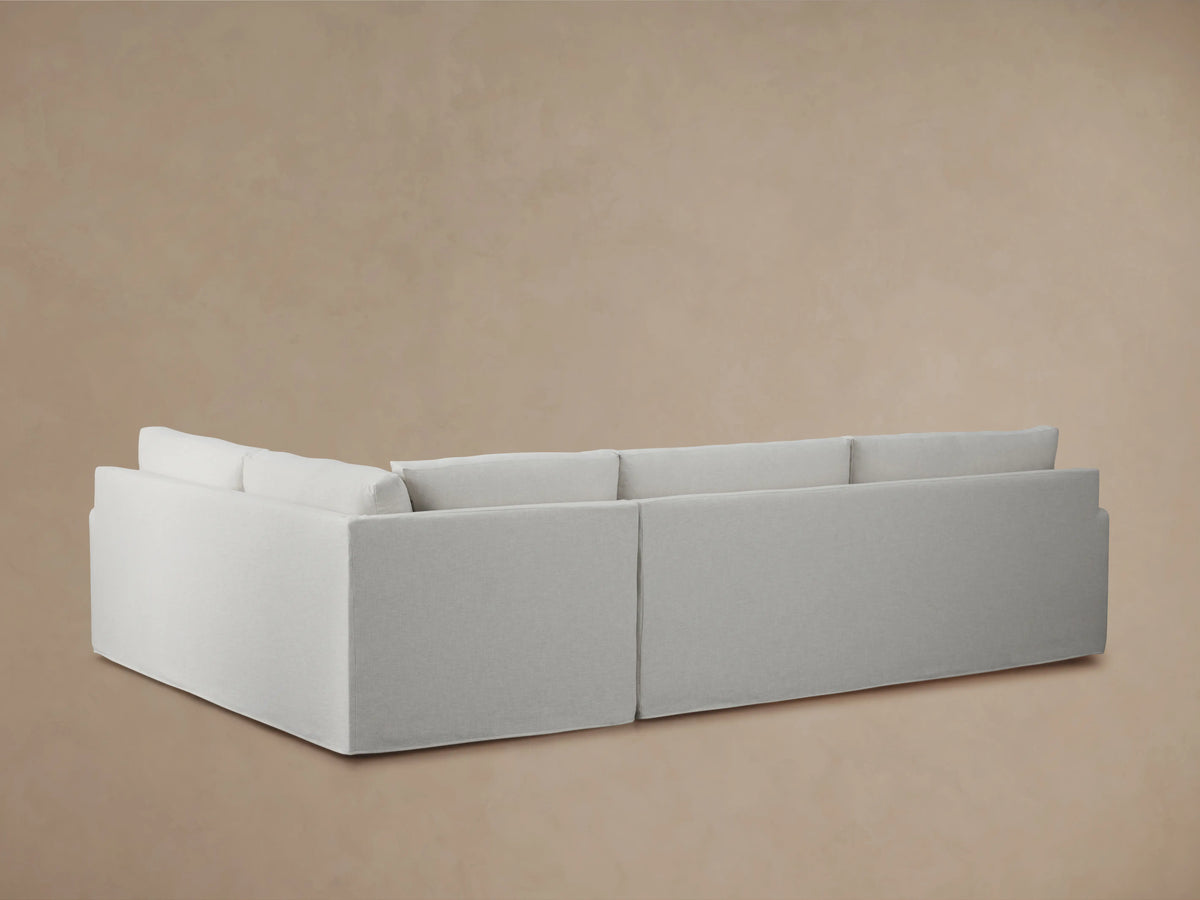 Kipton Slipcovered Two-Piece Sectional in light gray fabric, showing close-up of smooth armrest and plush seat cushions with a soft texture.