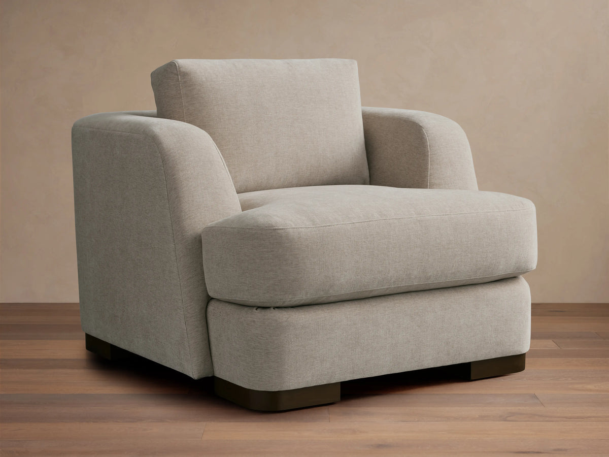 Beige upholstered Kayden Chair on a wooden floor, featuring a boxy design with thick, comfortable cushions and rounded armrests.