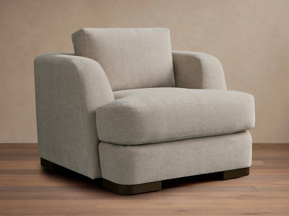 Beige upholstered Kayden Chair on a wooden floor, featuring a boxy design with thick, comfortable cushions and rounded armrests.