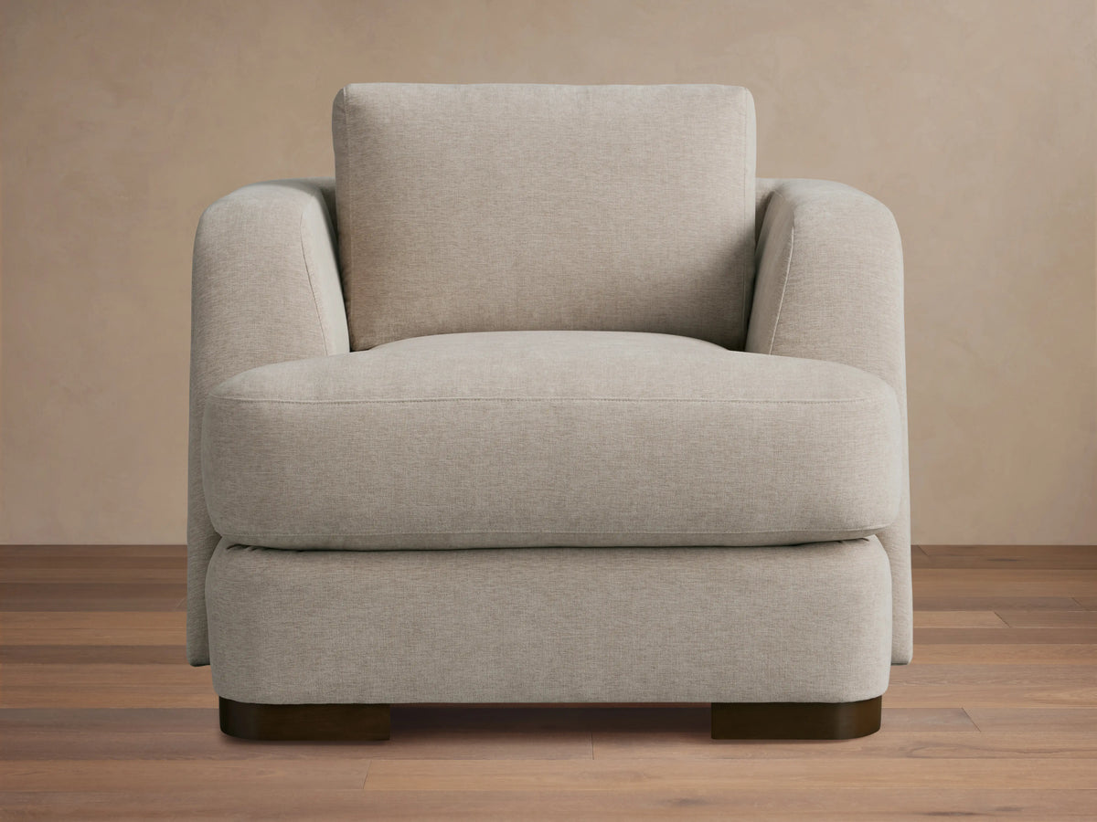 Beige upholstered Kayden Chair on a wooden floor, featuring a boxy design with thick, comfortable cushions and rounded armrests.