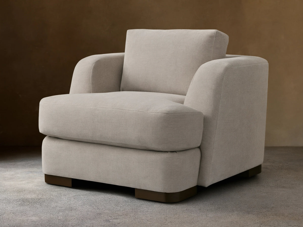 Beige upholstered Kayden Chair on a wooden floor, featuring a boxy design with thick, comfortable cushions and rounded armrests.