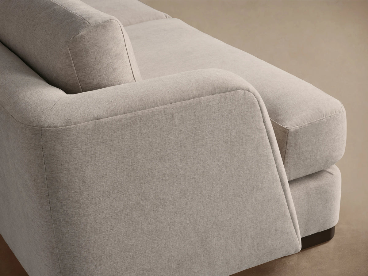 A beige, three-seater Kayden Sofa with clean lines, plush cushions, and slightly curved armrests, on a wooden floor.